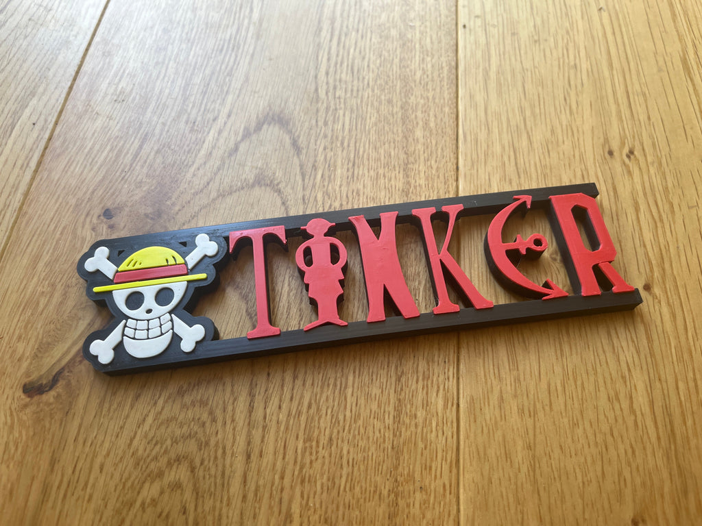 Decorative nameplate with 'TINKER' and skull design on a wooden surface